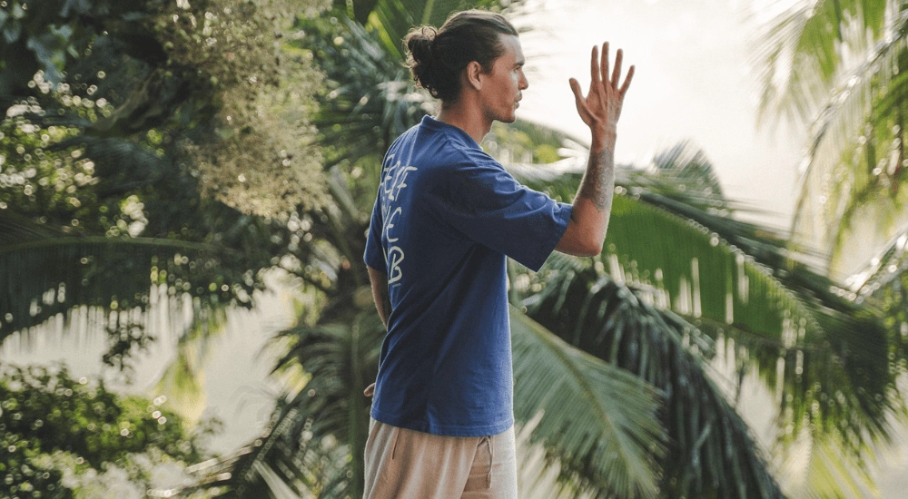 Ash performing an active meditation pose surrounded by palm trees and beautiful nature