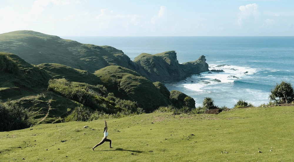 Woman performing yoga pose on a beautiful green cliff with the sea in the background.